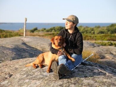 Nainen nauttii kalliolla istuen opaskoiransa kanssa