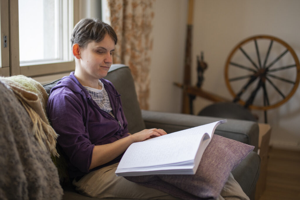 Kuva olohuoneesta. Nainen istumassa sohvalla lukemassa kirjaa.